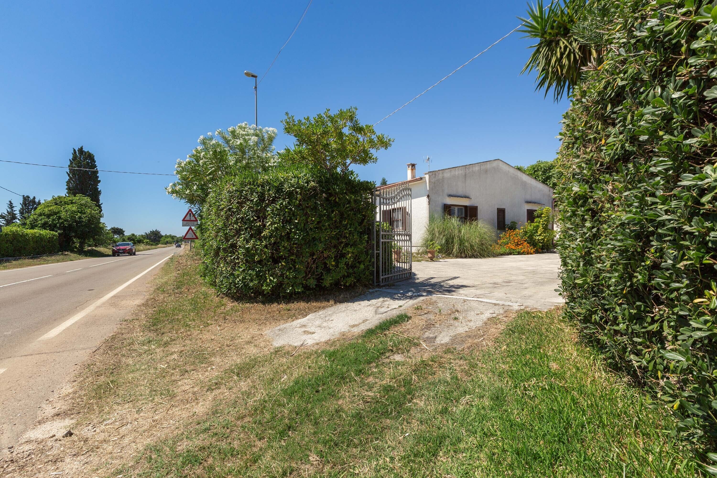 A rural road with a white building, a metal gate, and a sidewalk.