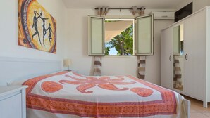 Un dormitorio con cama, armario, ventana con cortinas y un cuadro en la pared.