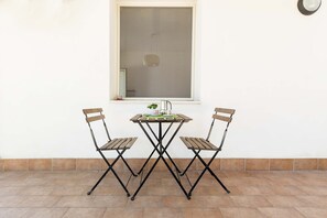 A small outdoor table with two chairs, a window above, and a tiled floor. - SoleDelSud - Monolocale by BarbarHouse (Laghi Alimini)