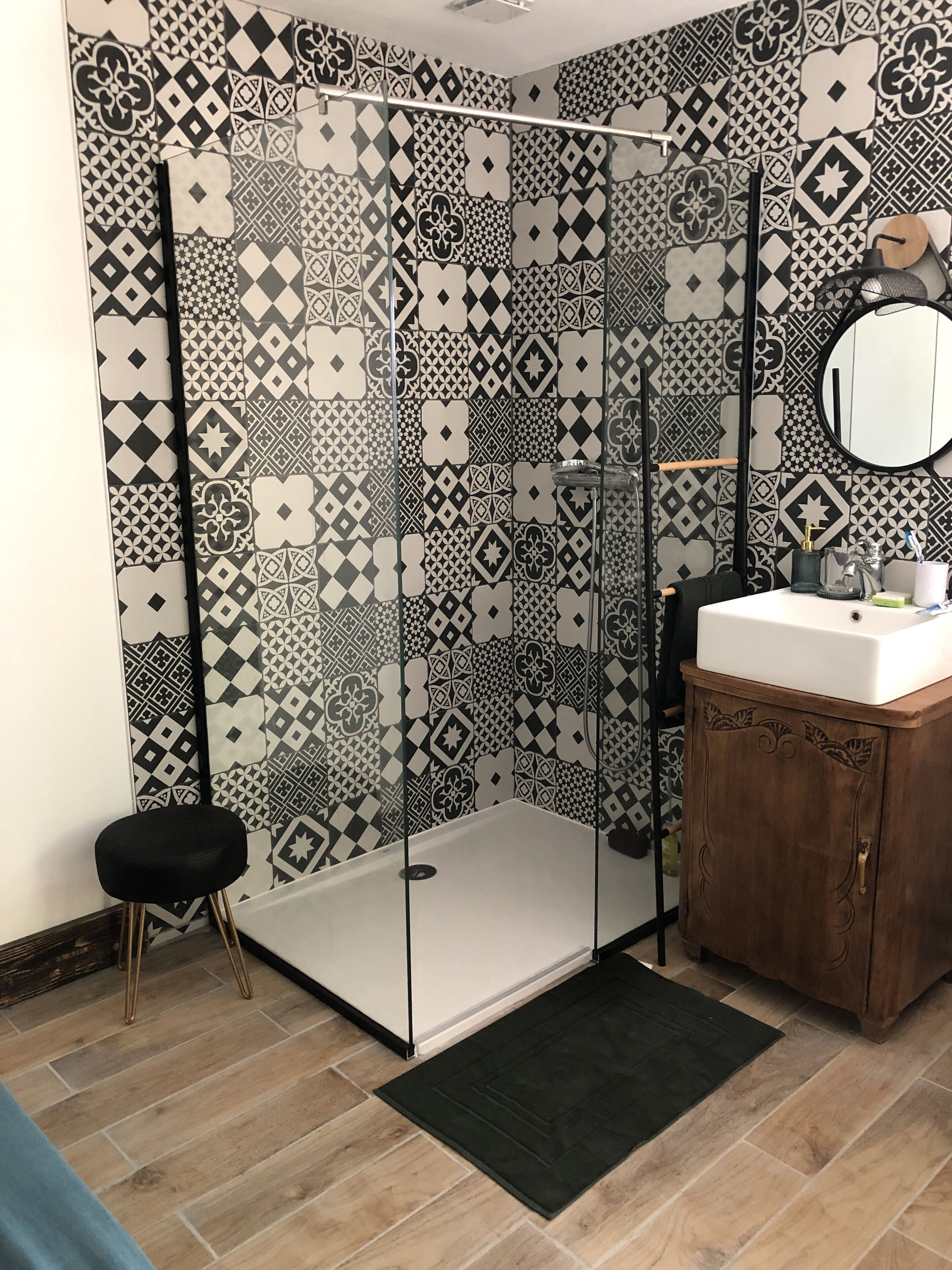 Un baño con ducha, lavamanos, espejo y azulejos con diseño.