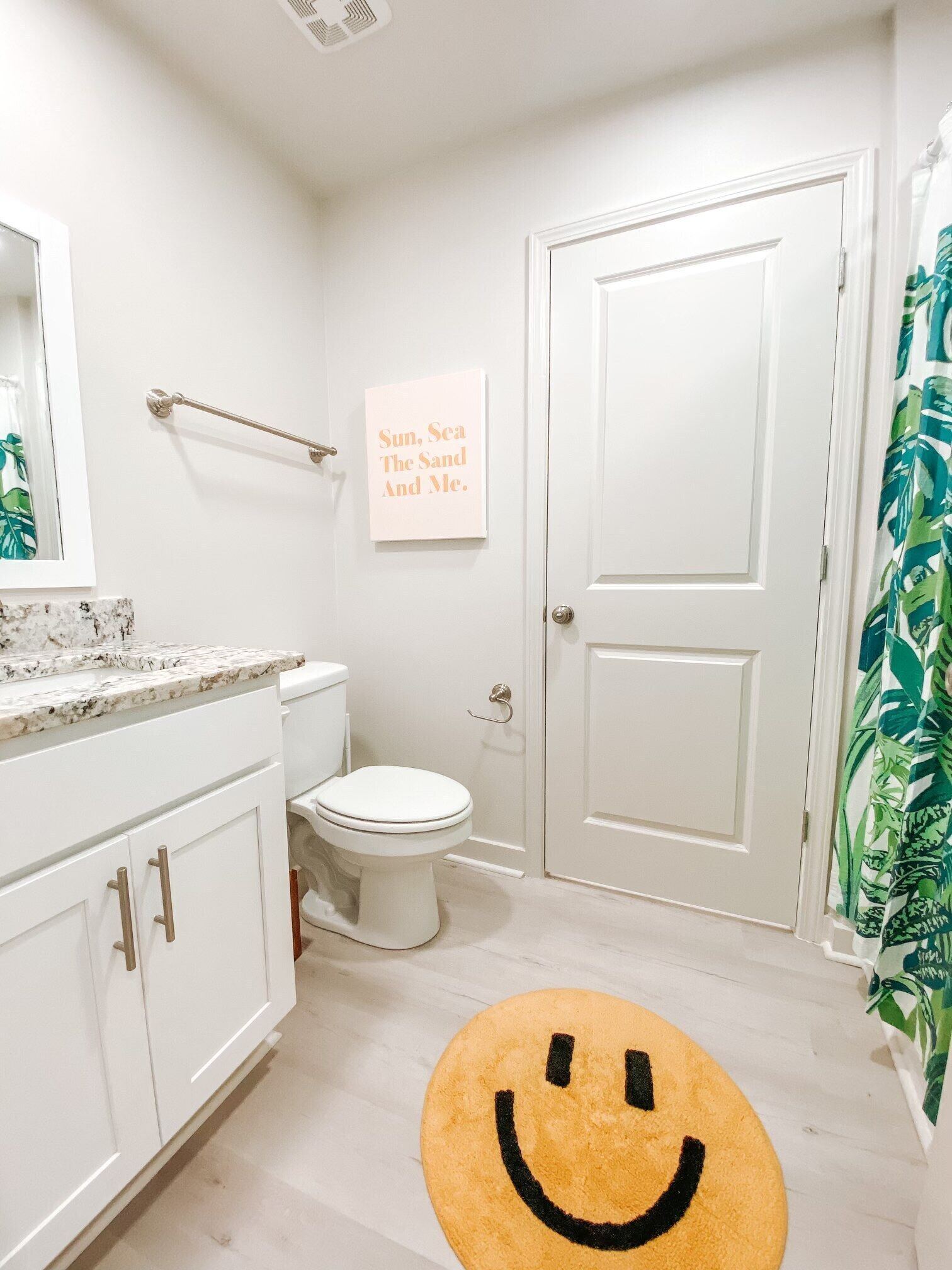 Ein Badezimmer mit Toilette, Waschbecken und Handtuchhalter. An der Wand ist ein Schild und auf dem Boden ein Teppich mit einem Smiley-Gesicht.