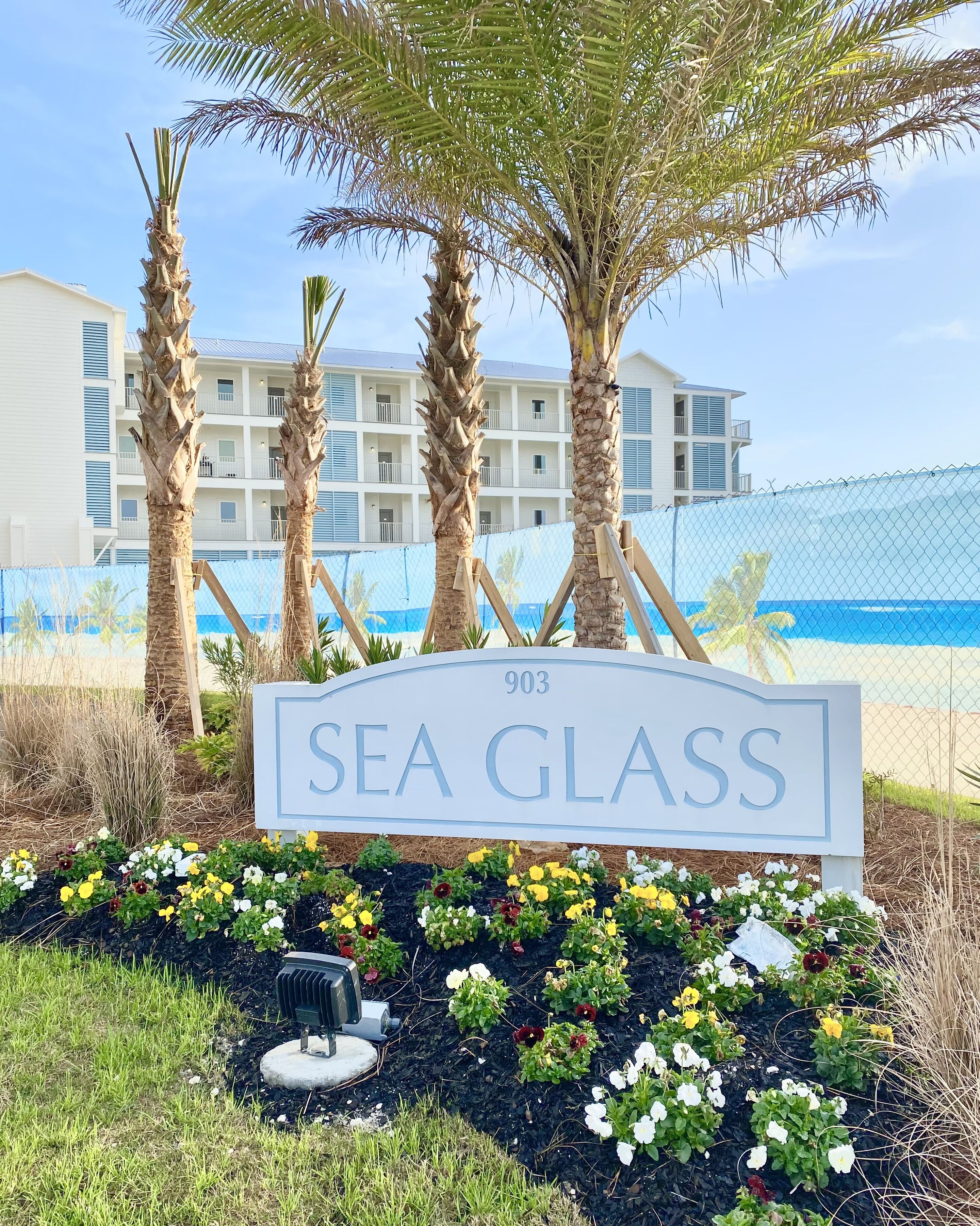 Señal que dice 'Sea Glass', con vista a un edificio y una valla al fondo.