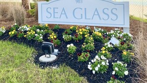 Señal que dice 'Sea Glass', con vista a un edificio y una valla al fondo.