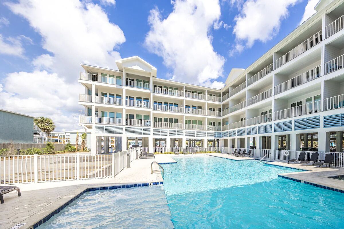 Un hotel con una gran piscina exterior, varios balcones y un cielo azul despejado.