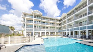 Un hotel con una gran piscina exterior, varios balcones y un cielo azul despejado.