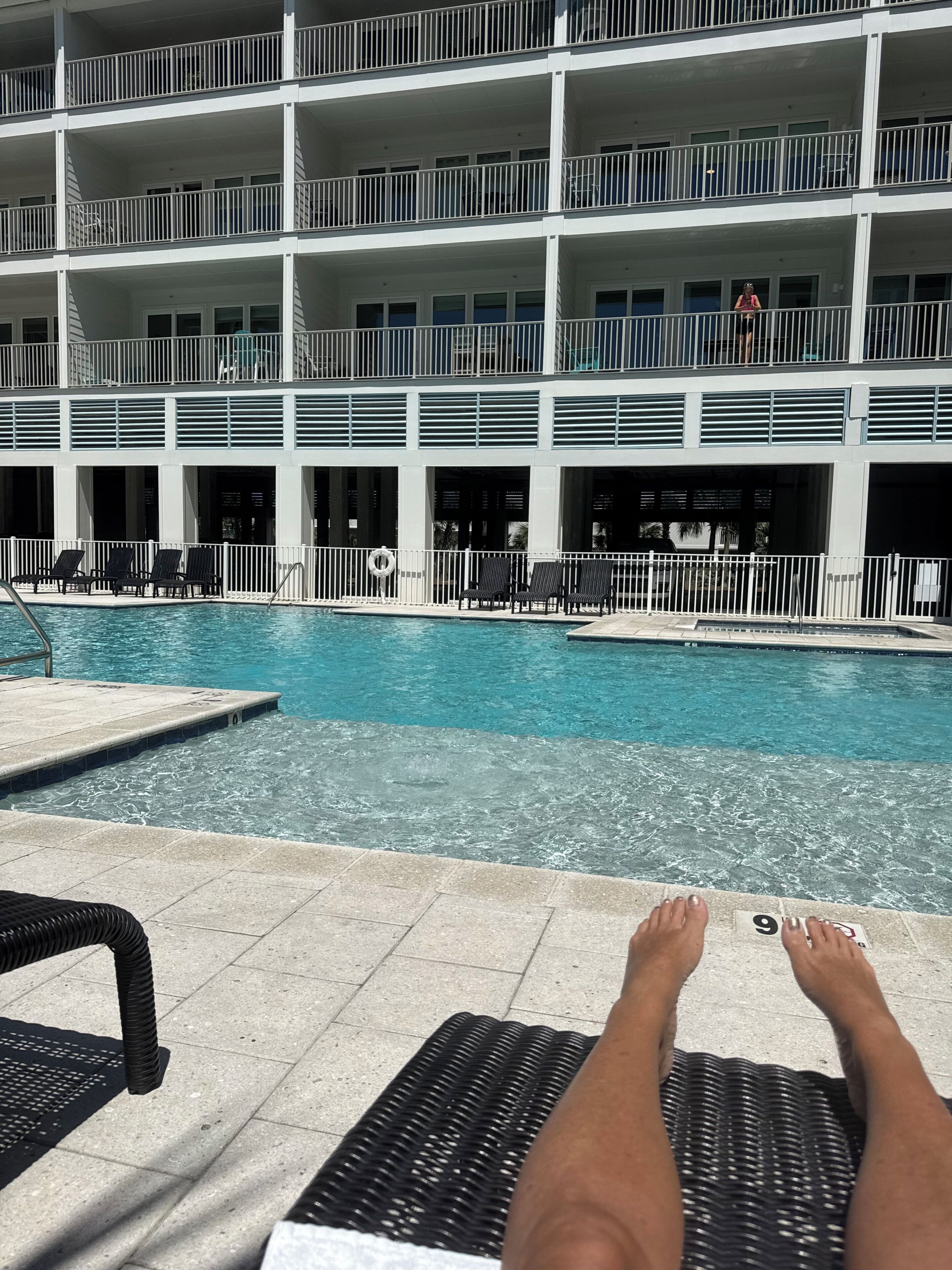 Une vue sur la piscine, avec un bâtiment à plusieurs niveaux, des chaises longues et une piscine à l’eau d’un bleu limpide.