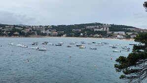Une ville côtière avec des bateaux sur l’eau, des bâtiments le long de la côte et un paysage vallonné en arrière-plan.
