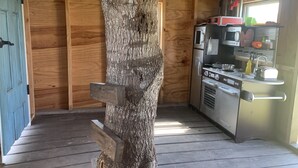 A rustic cabin interior with a wooden door, a tree trunk integrated into the structure, and a kitchenette with a microwave, toaster, and sink. - Entire House - Relax and Ride at Grace Ranch (Victoria)