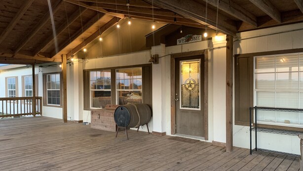 A wooden deck with a rustic barn-style entrance, a barrel, and a welcome sign. - Entire House - Relax and Ride at Grace Ranch (Victoria)