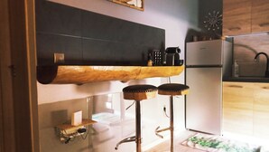 Ett kök med en trähylla, två barstolar, ett kylskåp och en klocka på väggen.