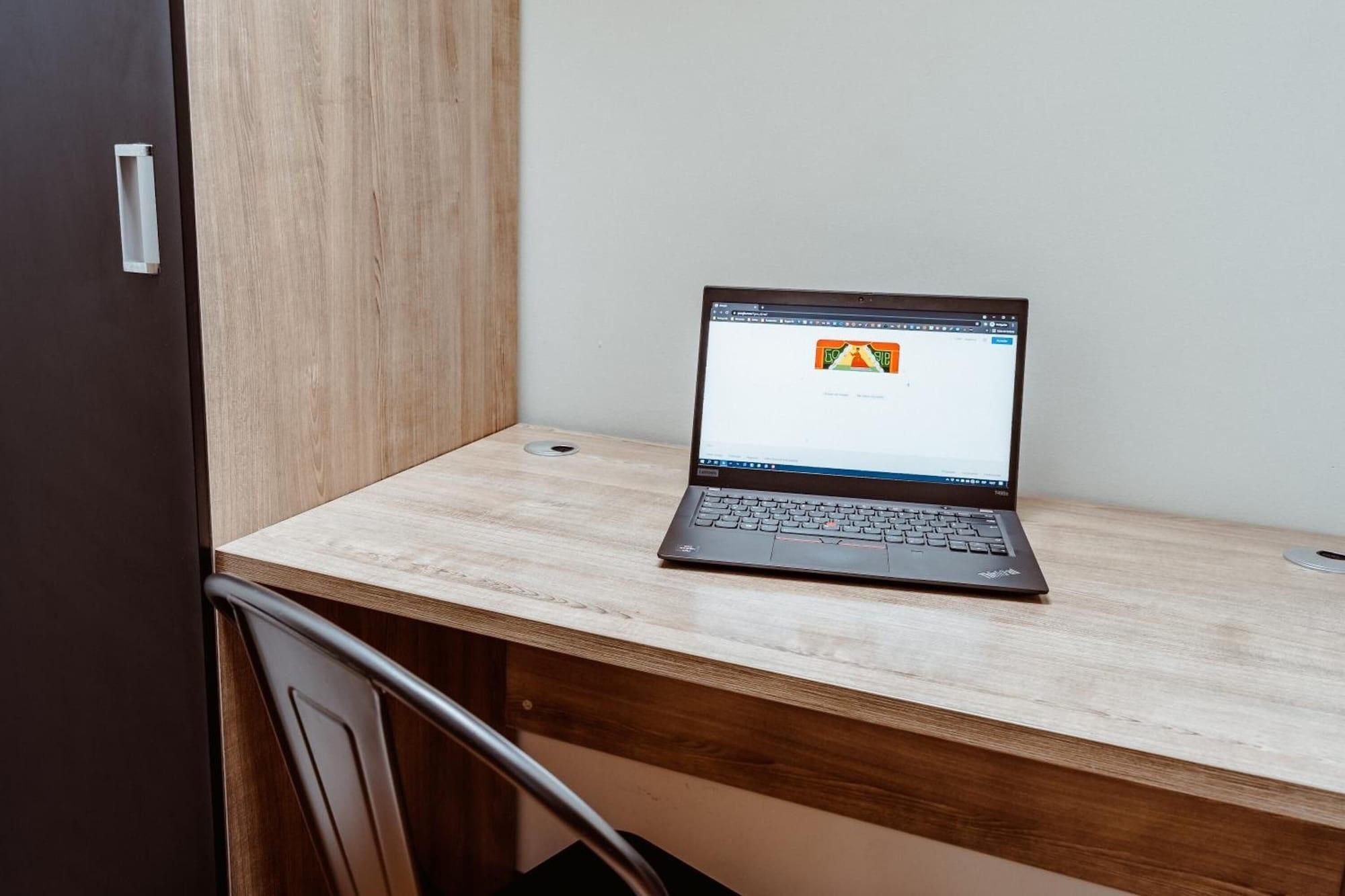 A laptop on a wooden desk with a door and a chair in the background.