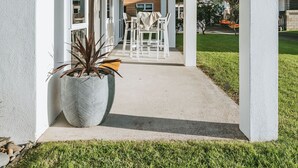 Ein überdachter Patio-Bereich mit Holzbalkendecke, weißen Säulen und einem großen Topfpflanzen.