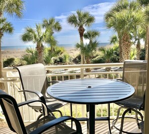 Una terraza con una mesa redonda y sillas que da a una playa con palmeras.