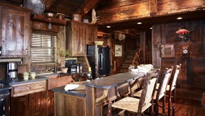 Une cuisine rustique en bois, avec une longue table à manger et des chaises, des armoires en bois et un luminaire suspendu.
