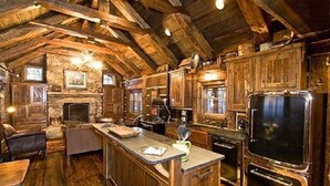 Une cuisine rustique avec des poutres en bois, une cheminée en pierre et un grand îlot central doté d’un évier et d’un plan de travail.