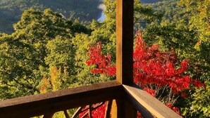 Un belvédère en bois agrémenté d’une fenêtre en vitrail, offrant une vue sur un paysage montagneux aux feuillages rouges.