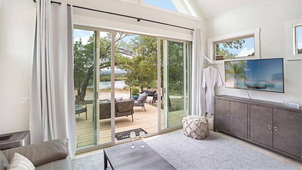Un salon moderne doté d’une porte-fenêtre coulissante donnant sur une terrasse, d’un téléviseur à écran plat fixé au mur et d’un coin salon confortable avec un canapé et une table basse.