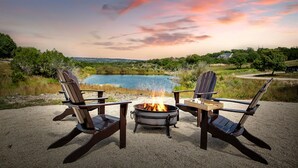 Deux fauteuils Adirondack sont placés face à un feu de camp, avec un lac et des arbres en arrière-plan.