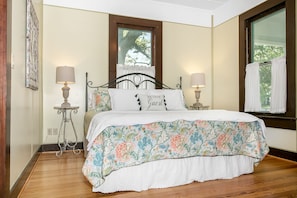 A neatly made bed with floral bedding, two bedside lamps, and a window with curtains.