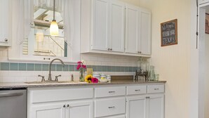 A kitchen with white cabinets, a granite countertop, a sink, and a chalkboard sign. - Oma Lange's Guesthouse | In Town | Hot Tub |  Full Kitchen | WiFi (Fredericksburg)