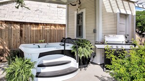 A backyard with a hot tub, a grill, and a wooden fence. - Oma Lange's Guesthouse | In Town | Hot Tub |  Full Kitchen | WiFi (Fredericksburg)
