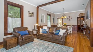A living room with leather sofas, a patterned rug, and a dining area with white chairs and a table. - Oma Lange's Guesthouse | In Town | Hot Tub |  Full Kitchen | WiFi (Fredericksburg)