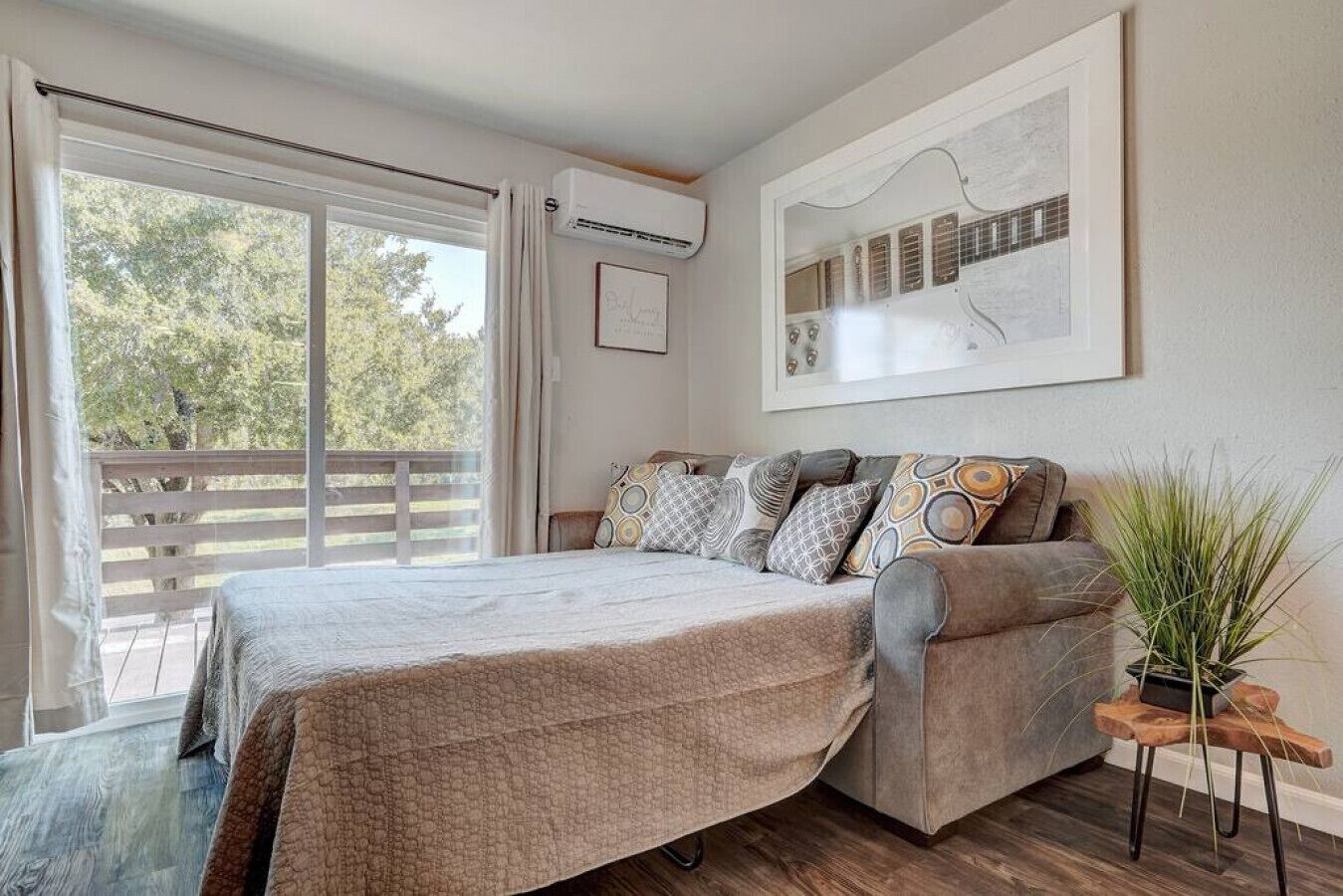 A bedroom with a bed, a sofa, a potted plant, and a framed picture on the wall.
