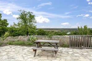 A picnic table on a stone patio with a view of a rural landscape and a wooden fence. - Jeffrey Spring- Starview | King Bed, Queen in Loft | Tranquil Country Setting | Hot Tub (Fredericksburg)