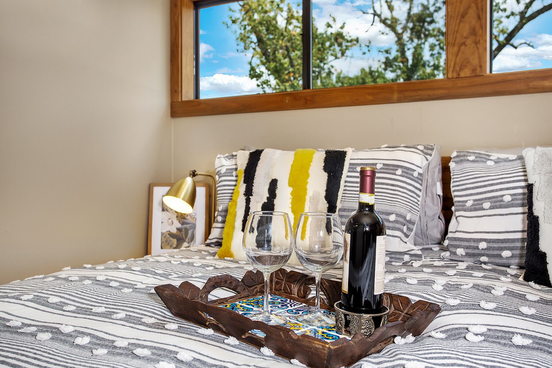 A bed with a bottle of wine, two glasses, and a tray.
