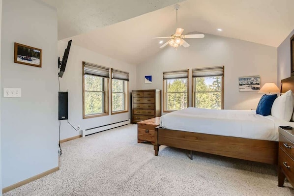 Une chambre à coucher avec un grand lit, deux fenêtres, un ventilateur de plafond et une commode.