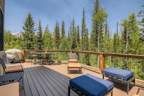 A wooden deck with outdoor furniture, including chairs and a table, overlooking a forested area. - 4BR Townhome w/ Private Hot Tub, Garage, and Deck (Silverthorne)
