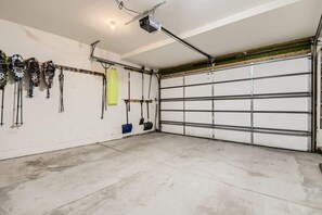A garage with a white door, ceiling-mounted lights, and various tools and helmets hanging on the wall.