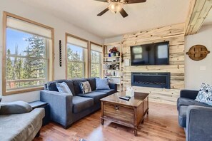 A cozy living room with a fireplace, large windows, and a TV mounted on the wall.