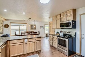 A spacious kitchen with wooden cabinets, a central island, stainless steel appliances, and a dining area with a table and chairs.