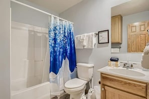 A bathroom with a white bathtub, a toilet, a sink with a mirror, and a shower curtain with a blue and white pattern. - 4BR Townhome w/ Private Hot Tub, Garage, and Deck (Silverthorne)