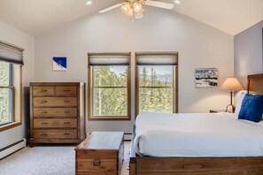 A bedroom with a bed, a dresser, a nightstand, and two windows with views of trees. - 4BR Townhome w/ Private Hot Tub, Garage, and Deck (Silverthorne)