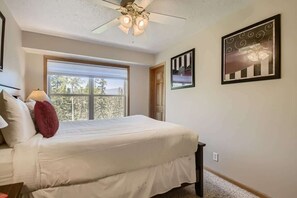 A bedroom with a bed, a ceiling fan, a window, and framed artwork on the wall.