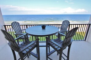 Une table ronde entourée de quatre chaises Adirondack sur un balcon donnant sur l’océan.