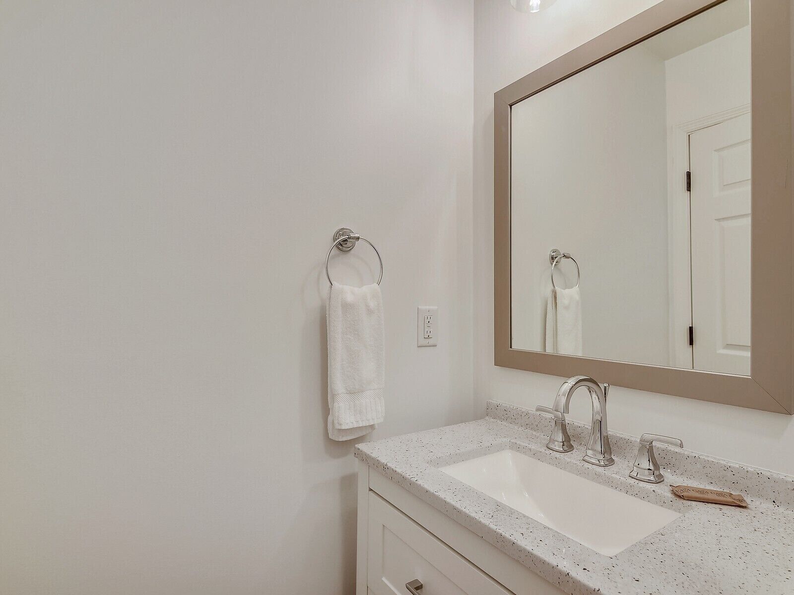A bathroom with a white sink, two faucets, a large mirror, and a towel rack.