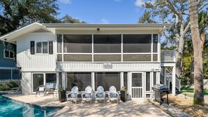 Une maison à deux étages dotée d’un porche grillagé, d’une piscine et d’un panneau indiquant « Propriété en bord de mer ».