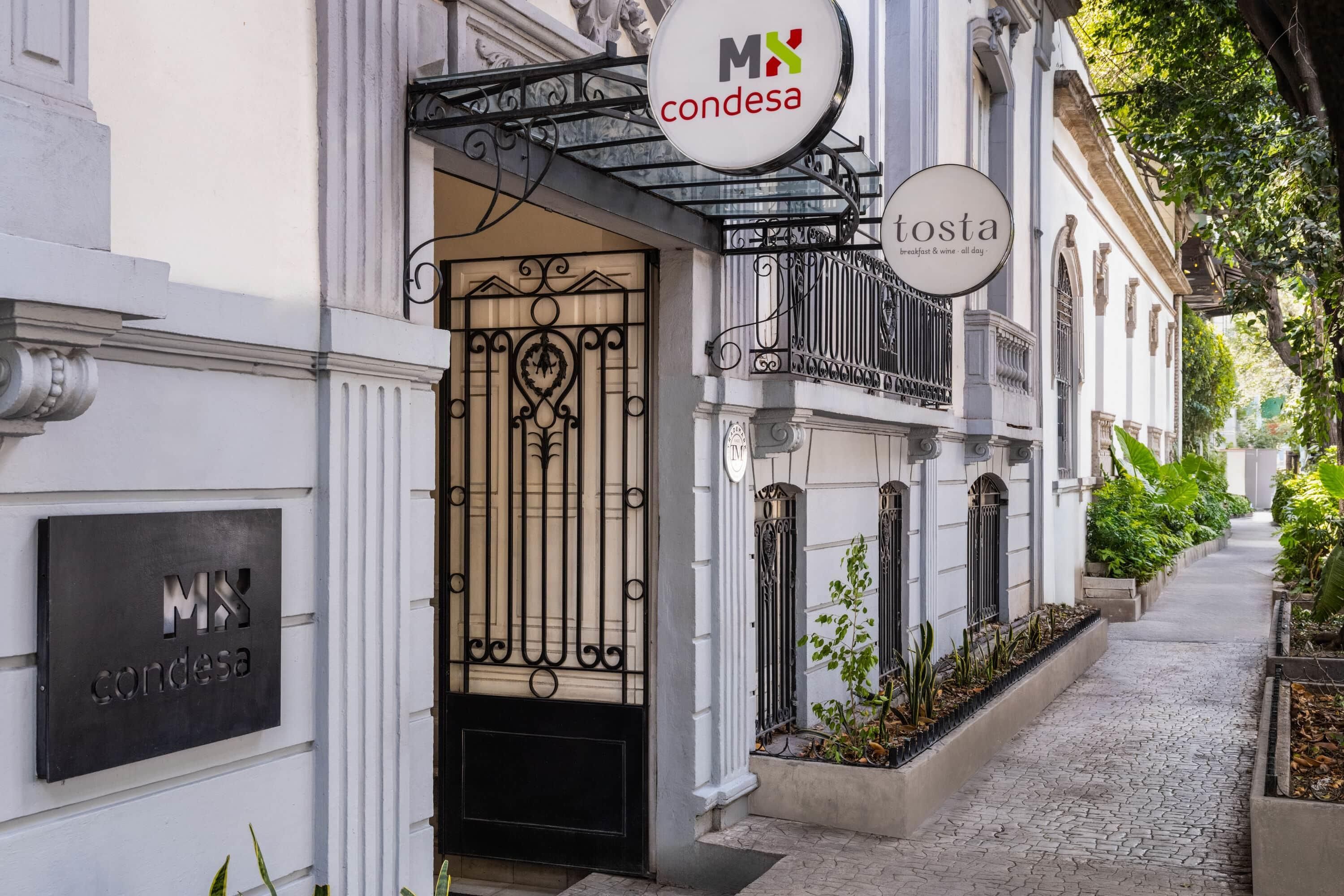 A building with a wrought iron gate, a sign for 'MX Condesa', and a sign for 'tosta breakfast & wine - all day'.