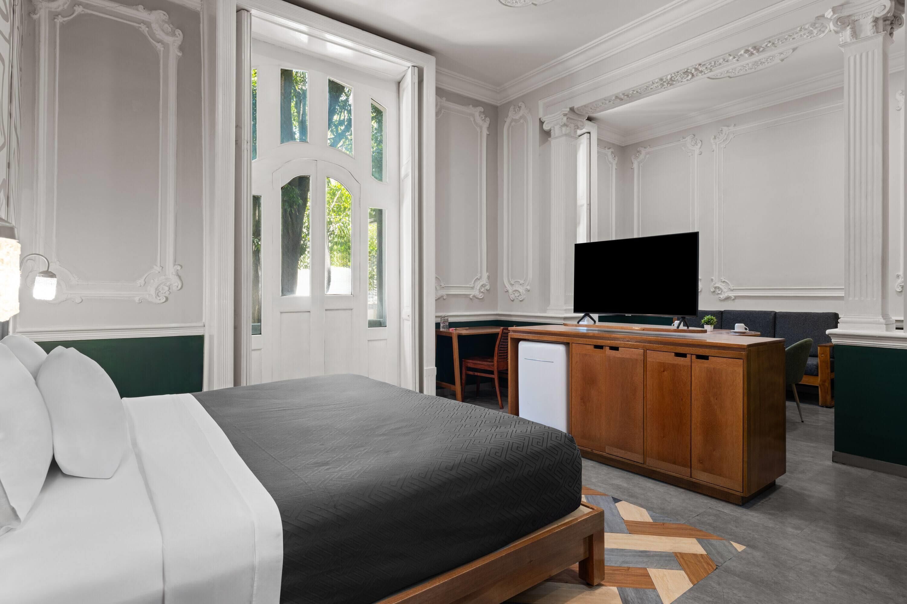 Habitación de hotel moderna con cama, televisión, kitchenette y vistas a zonas verdes.