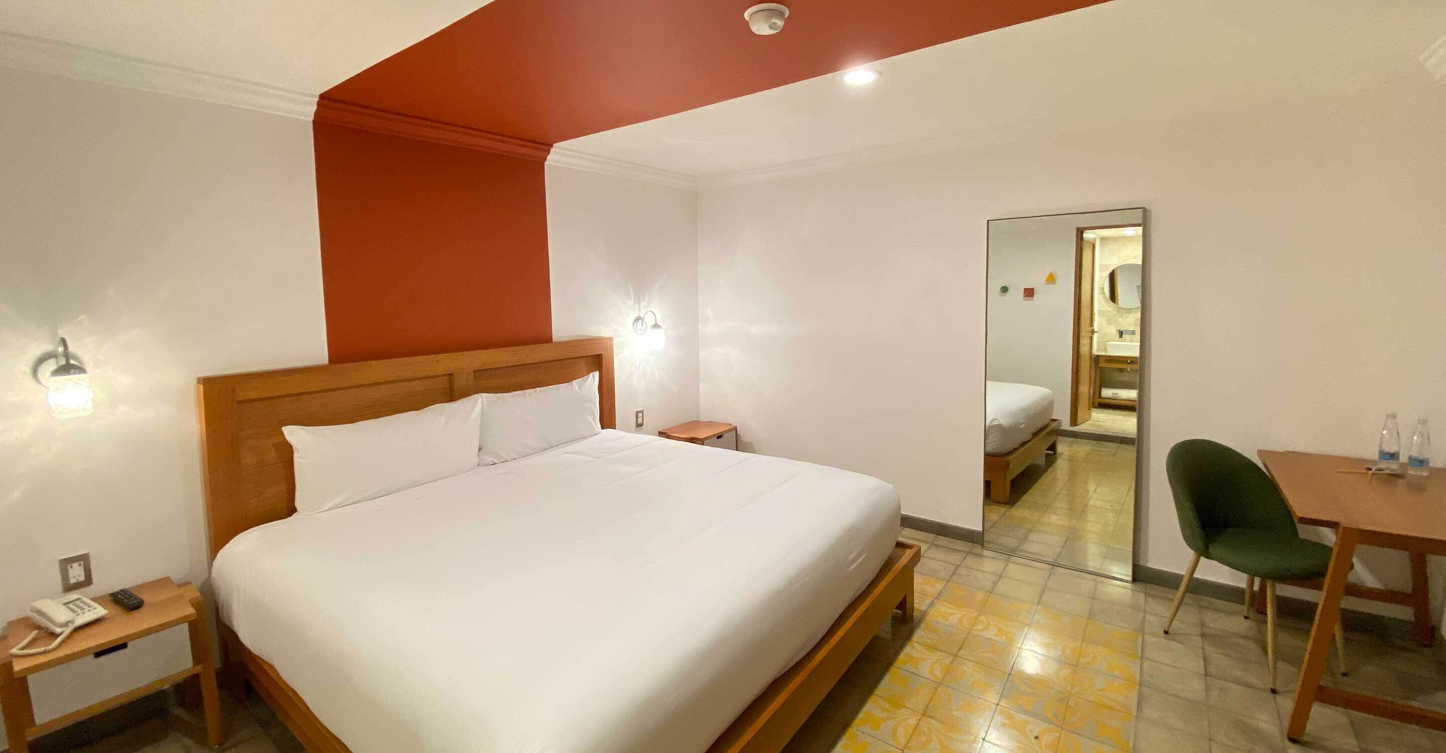 Une chambre d’hôtel avec un grand lit, une table de chevet avec un téléphone, un bureau avec une chaise et un miroir.
