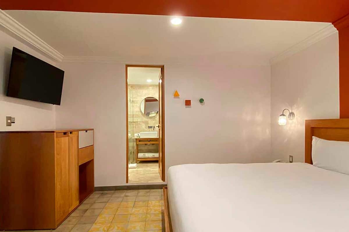 Hotelkamer met een bed, een aan de muur bevestigde televisie, een houten bureau en een badkamer zichtbaar door een geopende deur.