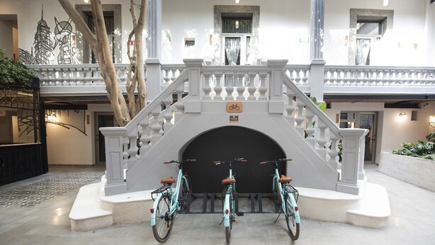 Un grand escalier, avec un porte-vélos à sa base, est entouré d’un vaste espace intérieur doté d’un sol carrelé et d’un balcon agrémenté de plantes.