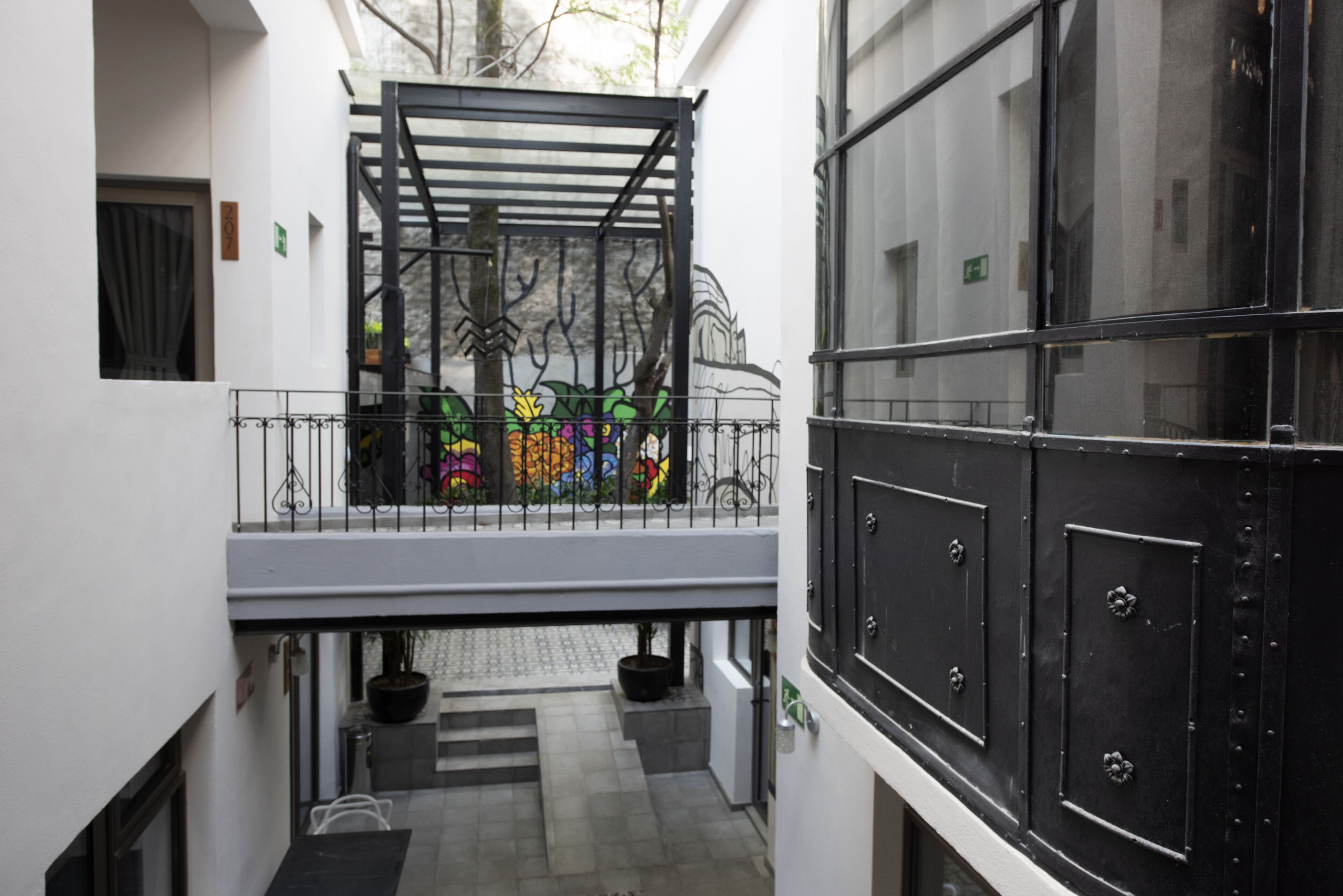 A narrow corridor with a metal railing, a staircase, and a black door with decorative elements.
