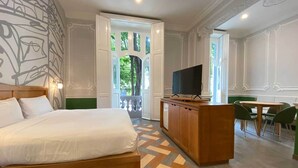 Une chambre d’hôtel avec un grand lit, un bureau en bois, une télévision et un coin repas avec des chaises.