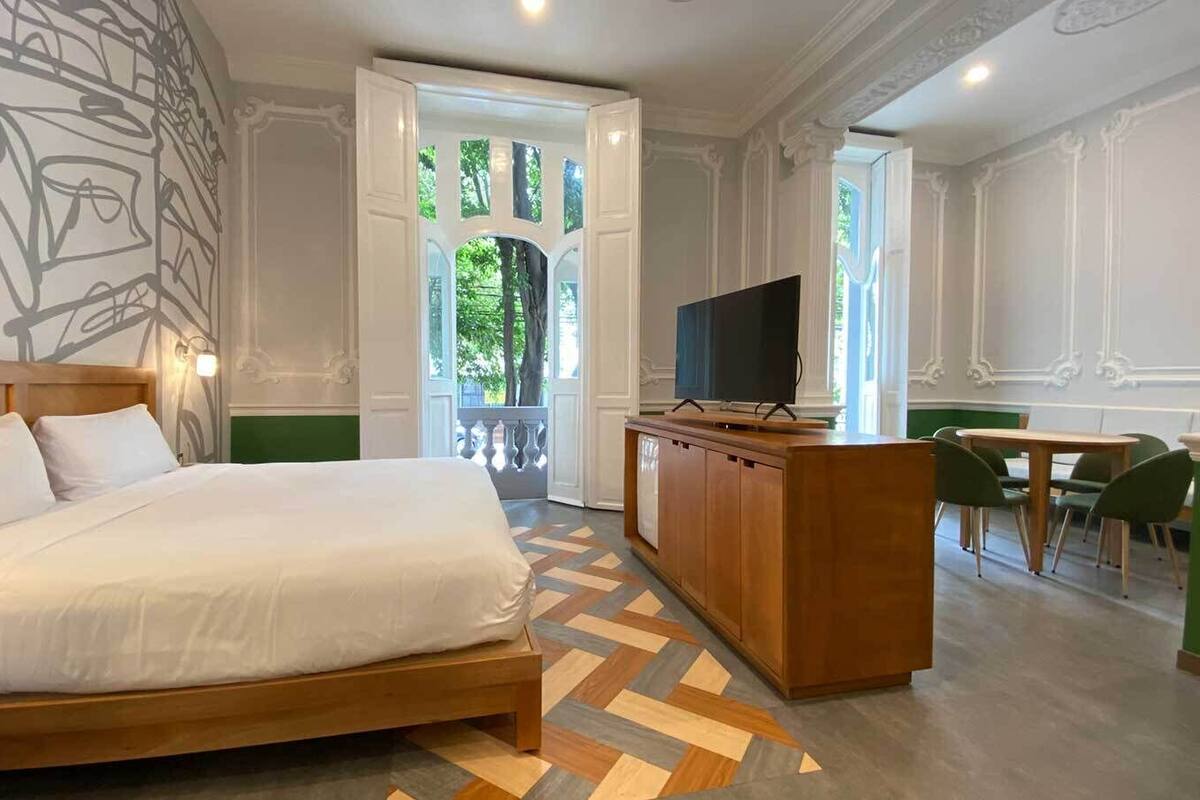 Een hotelkamer met een groot bed, een houten bureau, een televisie en een zithoek met stoelen.
