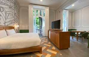 Habitación de hotel con una cama grande, un escritorio de madera, televisor y un área de comedor con sillas.