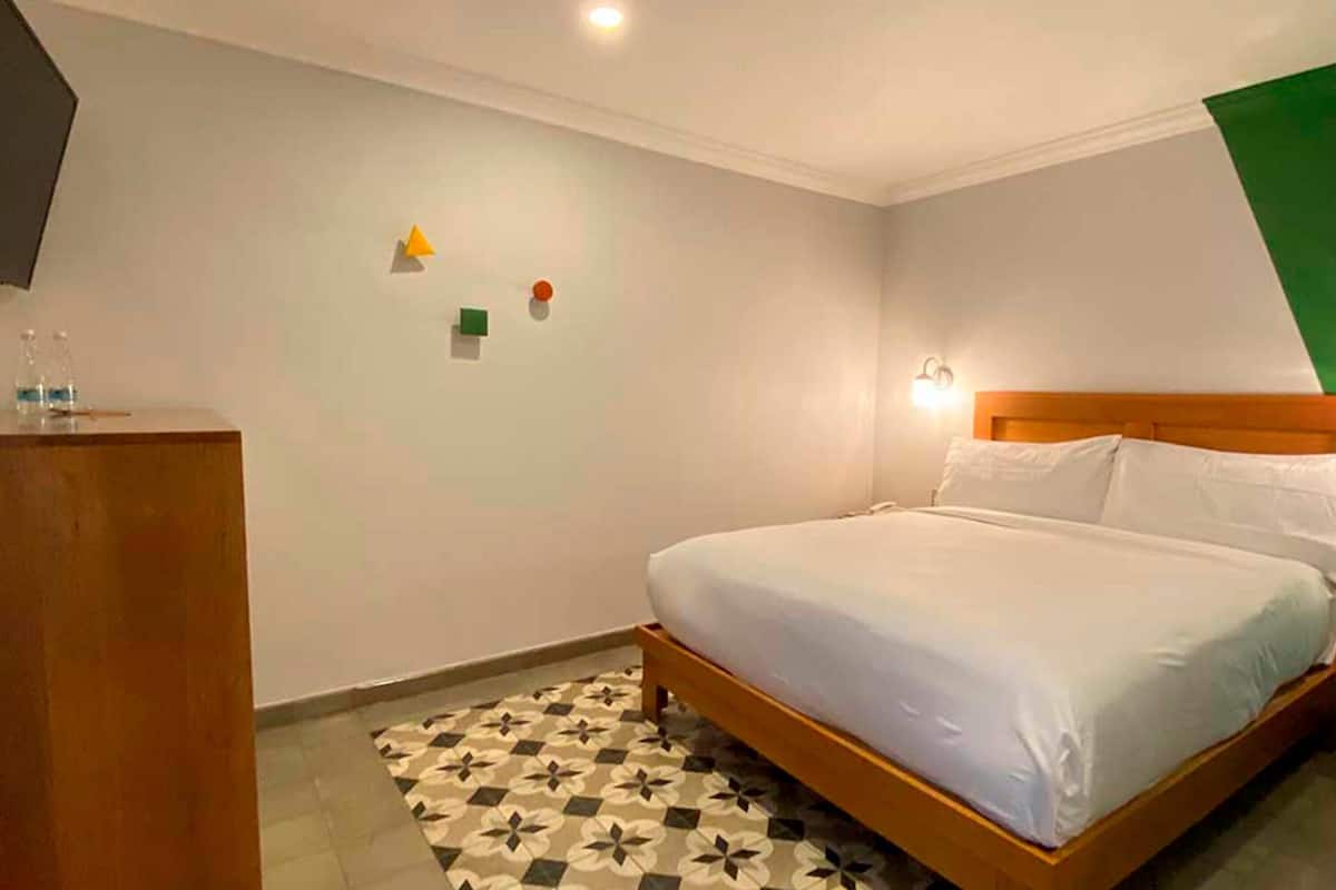 Een hotelkamer met een bed, een houten hoofdbord, een klein bureau en een kamerbreed tapijt met patroon.